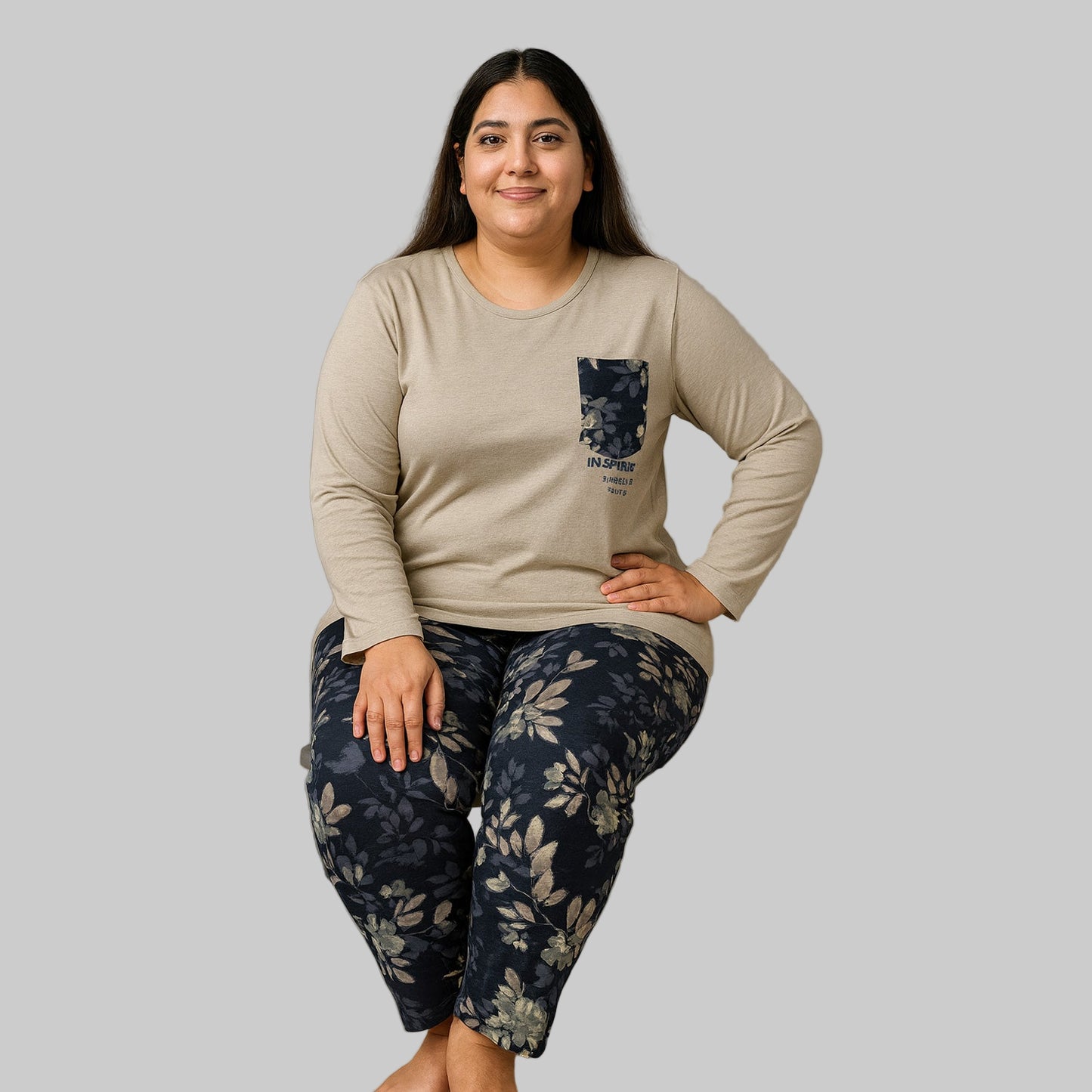 Plus-size woman wearing a beige long-sleeve pajama top with floral pocket and black floral print pajama bottoms — cozy cotton-blend sleepwear set.