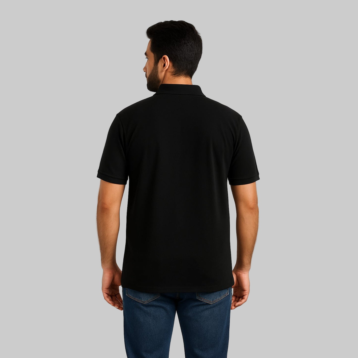 Plus-size Pakistani male model wearing black piqué polo shirt with dark jeans on a light studio background, relaxed fit.