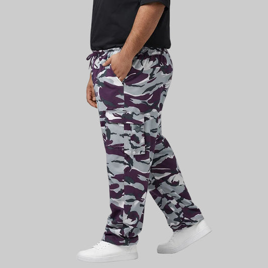 Camo Charge plus-size terry cargo pants worn by a Pakistani male model in a side pose, featuring a purple, grey, white, and black camouflage print with elastic waistband and side cargo pockets.
