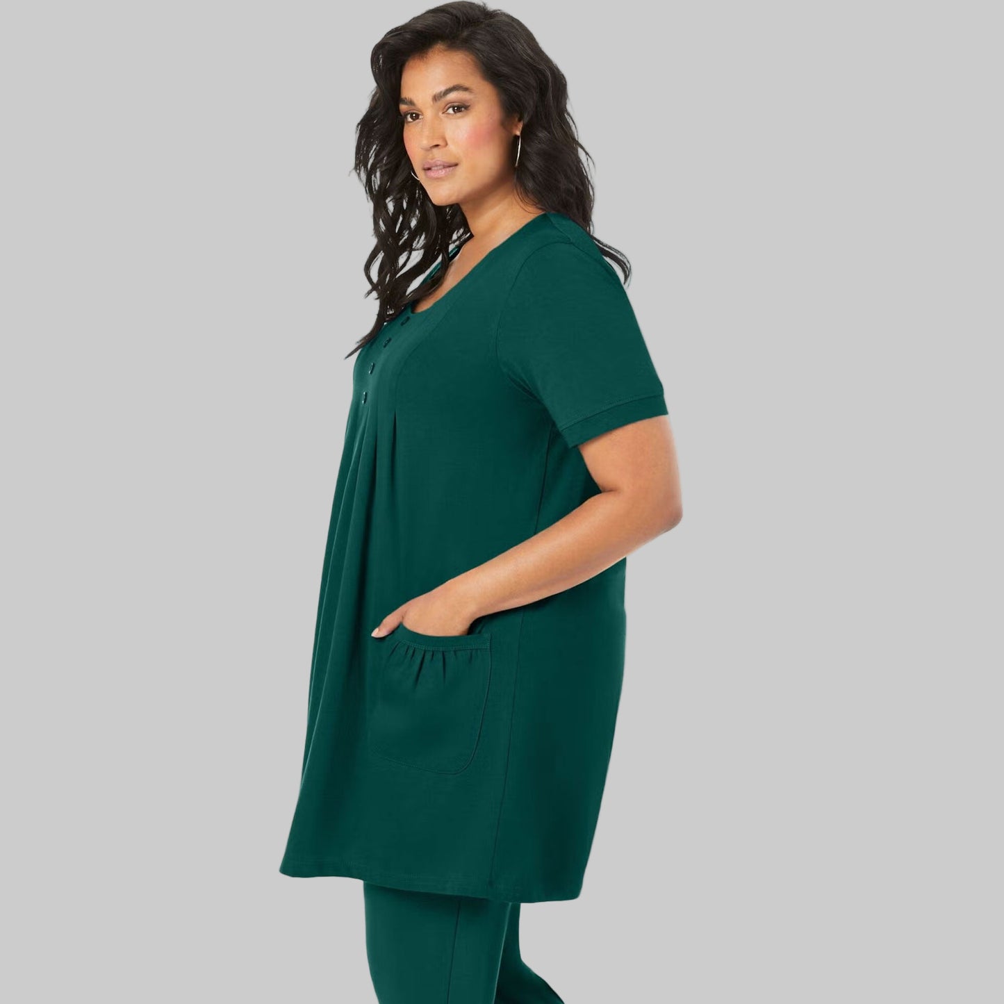 Emerald green knit women’s tunic with two front pockets, draped on a hanger with a white background