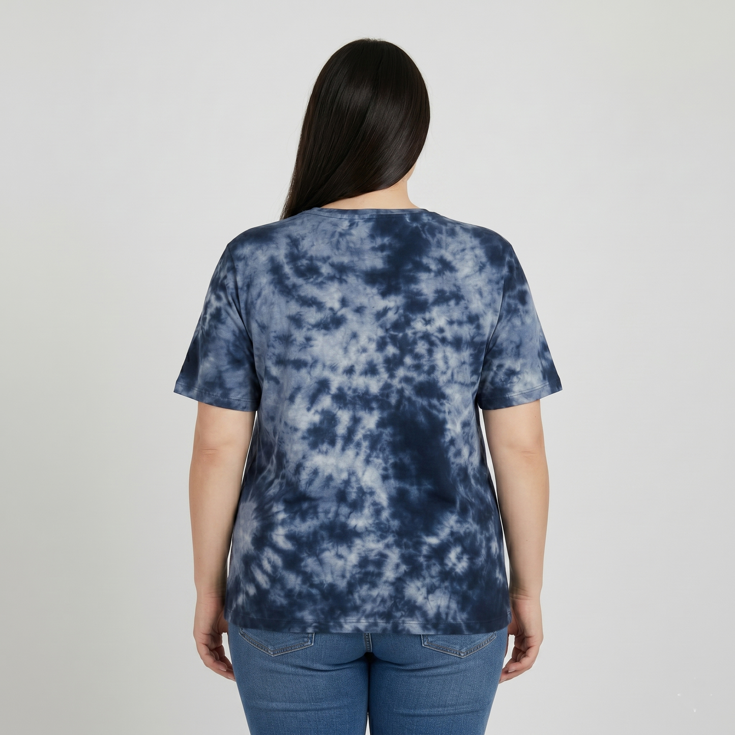 Person wearing a blue tie-dye t-shirt and jeans on a plain background