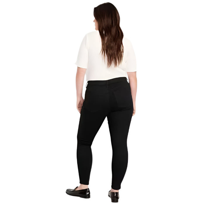 Plus-size model wearing black wash mid rise super skinny jeans with button front, zip fly, and front/back pockets, standing against a white background.