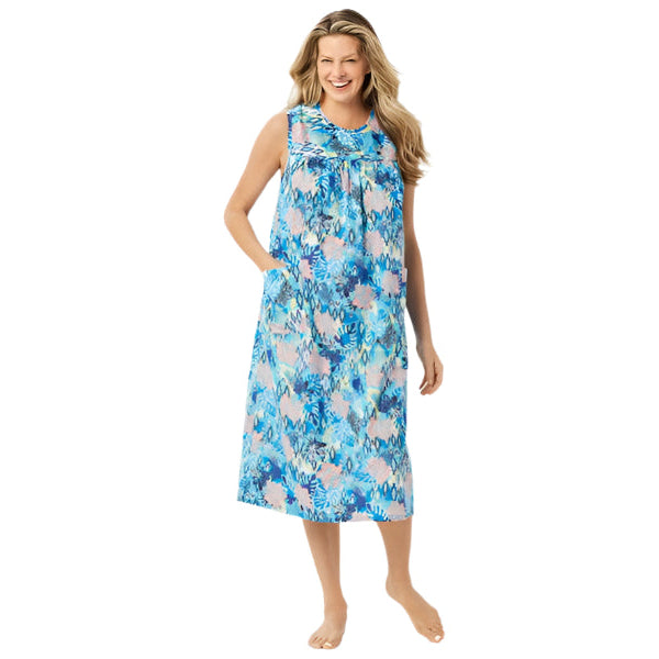 Plus-size woman wearing a sleeveless, mid-length lounger with a vibrant tropical palm print, featuring shirred front and back yokes and front patch pockets.