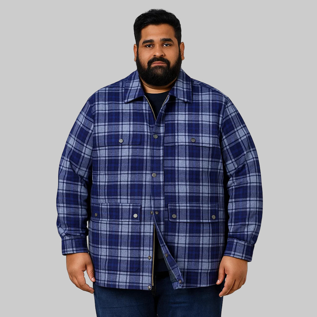 Plus-size man wearing a navy plaid zip-front shirt jacket with quilted lining, chest pockets, and storm flap, standing against a clean white studio background.