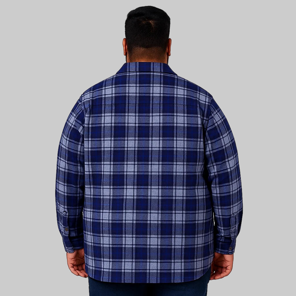 Plus-size man wearing a navy plaid zip-front shirt jacket with quilted lining, chest pockets, and storm flap, standing against a clean white studio background.