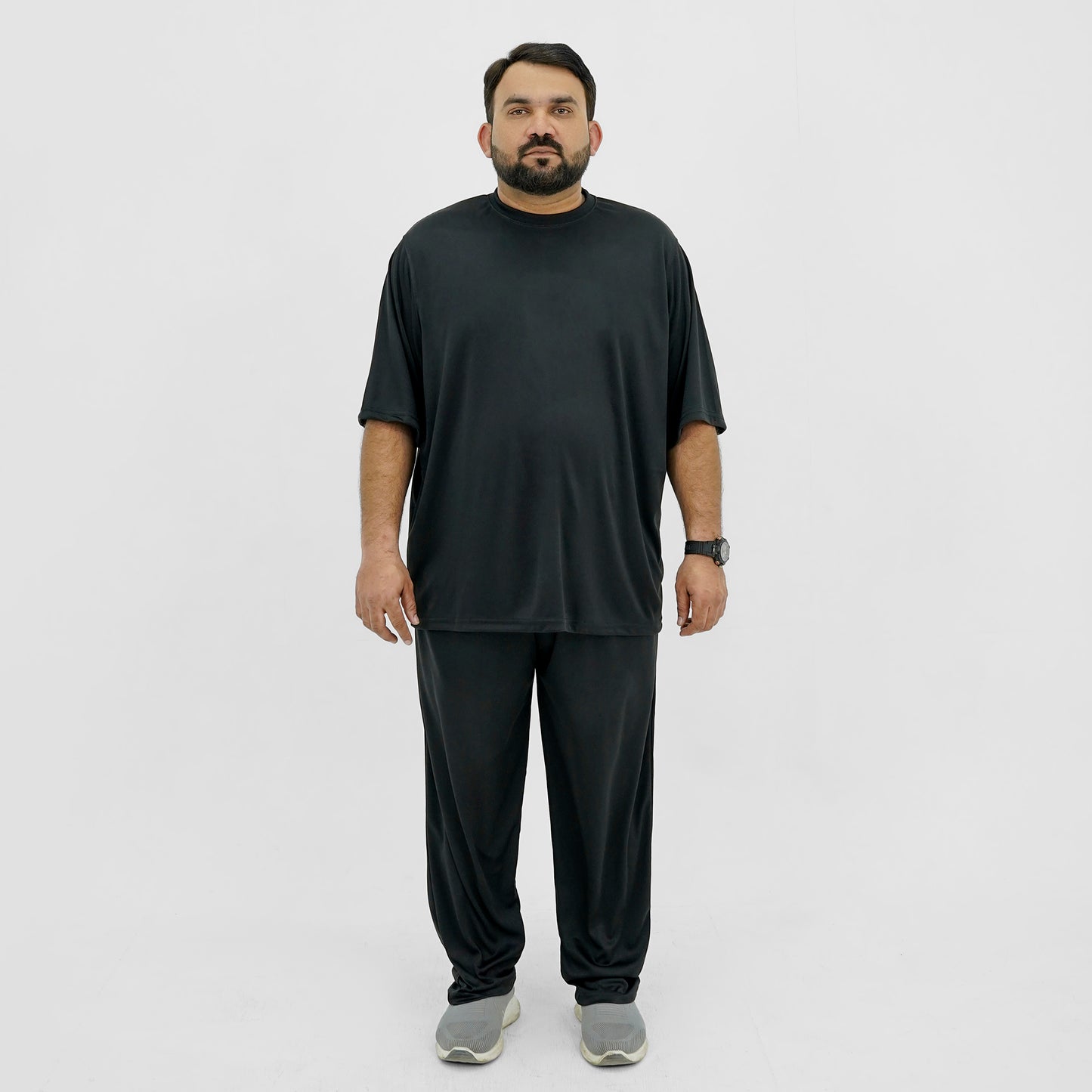 A plus size man wearing a black t-shirt and black pants standing against a white background.