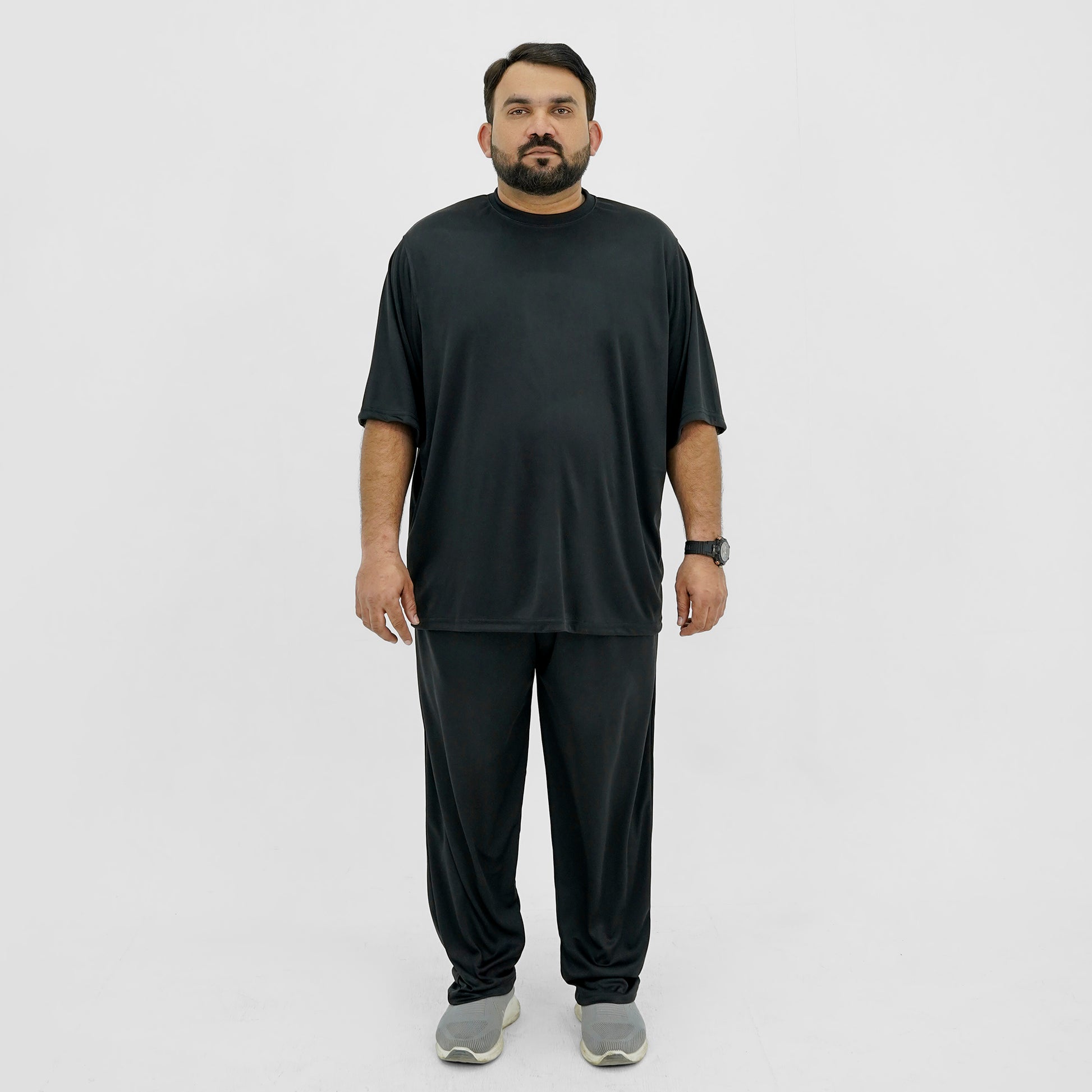 A plus size man wearing a black t-shirt and black pants standing against a white background.