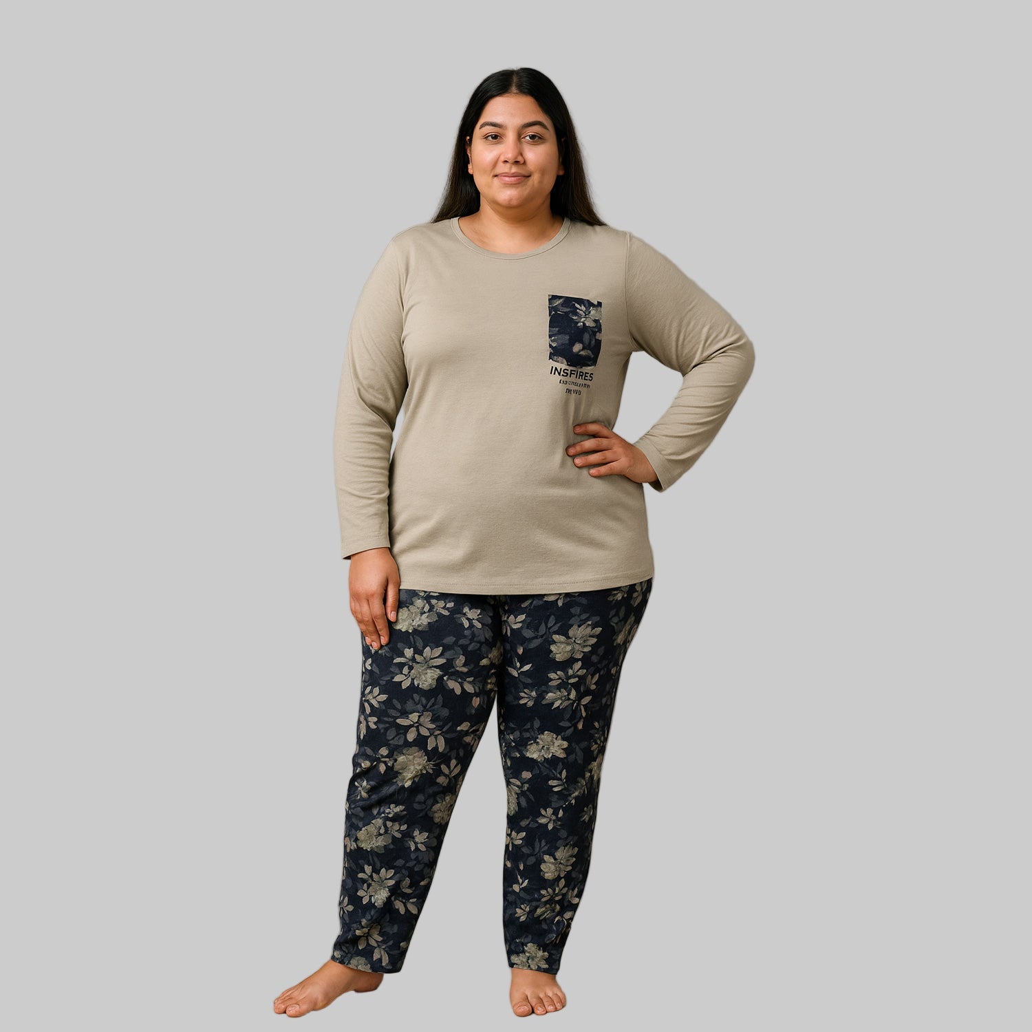 Plus-size woman wearing a beige long-sleeve pajama top with floral pocket and black floral print pajama bottoms — cozy cotton-blend sleepwear set.