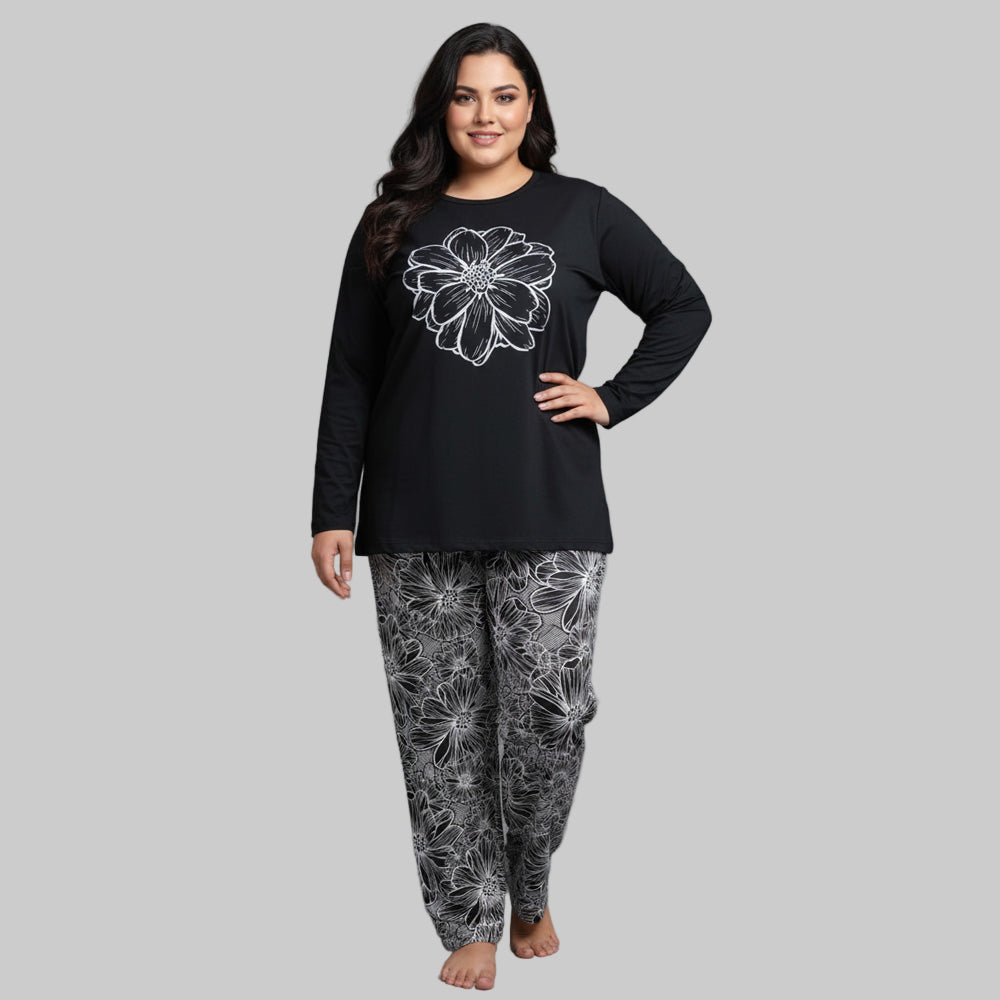 Plus-size woman wearing a black long-sleeve top with white floral graphic and matching floral print pajama bottoms — cozy cotton-blend sleepwear set.