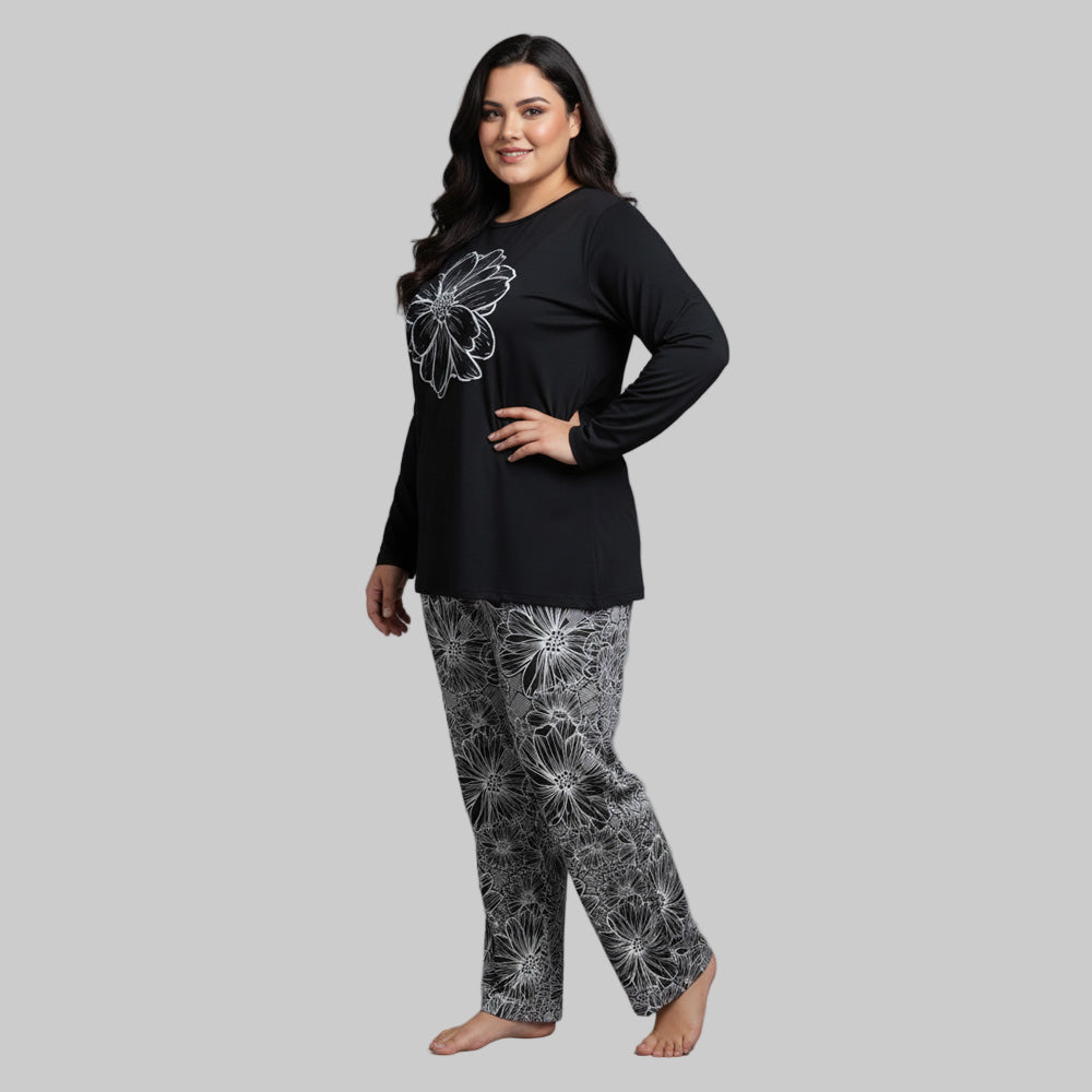 Plus-size woman wearing a black long-sleeve top with white floral graphic and matching floral print pajama bottoms — cozy cotton-blend sleepwear set.