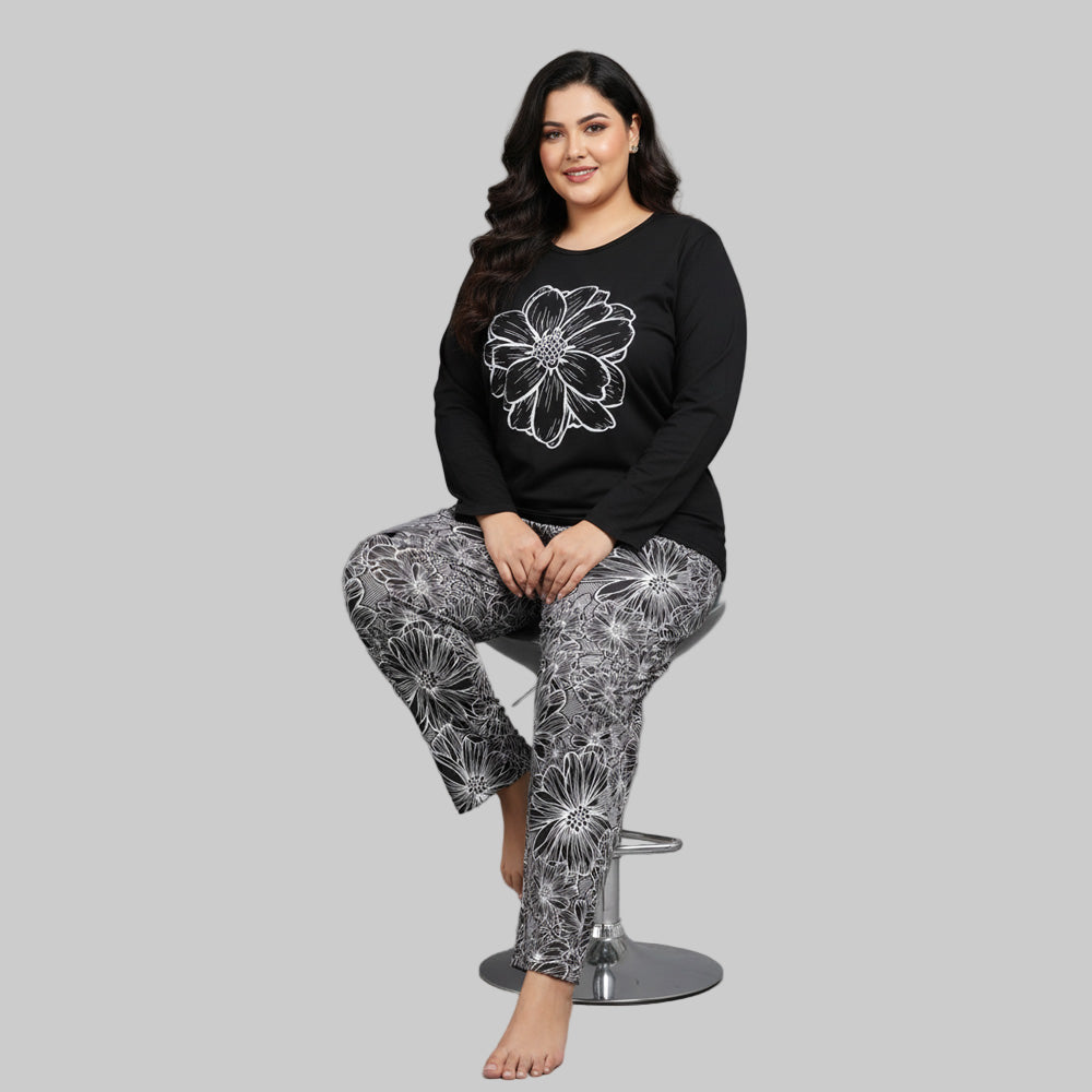 Plus-size woman wearing a black long-sleeve top with white floral graphic and matching floral print pajama bottoms — cozy cotton-blend sleepwear set.