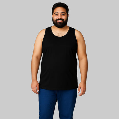 Plus-size Pakistani male model wearing a black sleeveless cotton tank top with dark jeans on a light-gray background, relaxed fit casual wear.