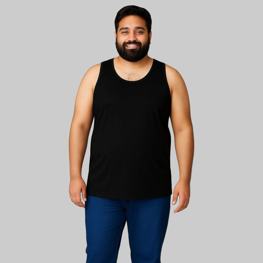 Plus-size Pakistani male model wearing a black sleeveless cotton tank top with dark jeans on a light-gray background, relaxed fit casual wear.