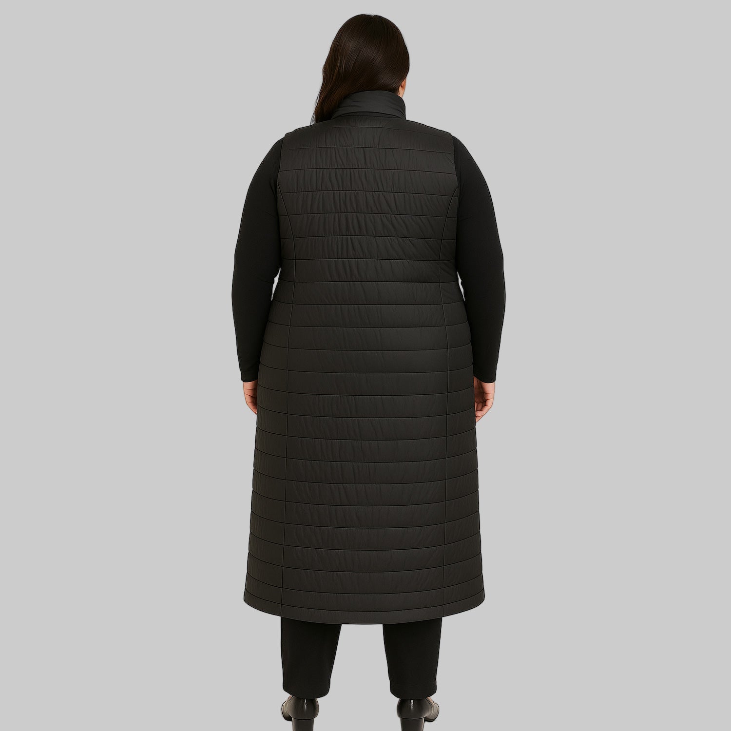 Plus-size female model wearing a long black quilted puffer sleeveless jacket with a zip-front closure, front view.