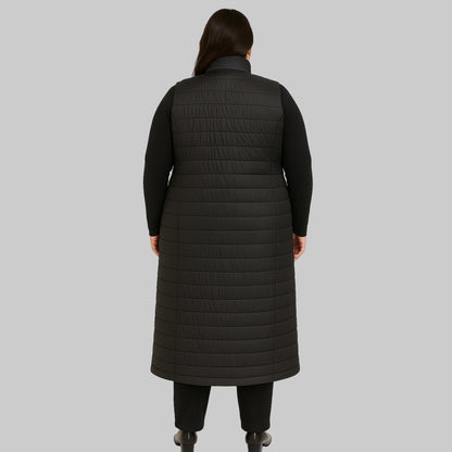 Plus-size female model wearing a long black quilted puffer sleeveless jacket with a zip-front closure, front view.