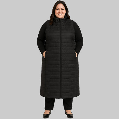 Plus-size female model wearing a long black quilted puffer sleeveless jacket with a zip-front closure, front view.