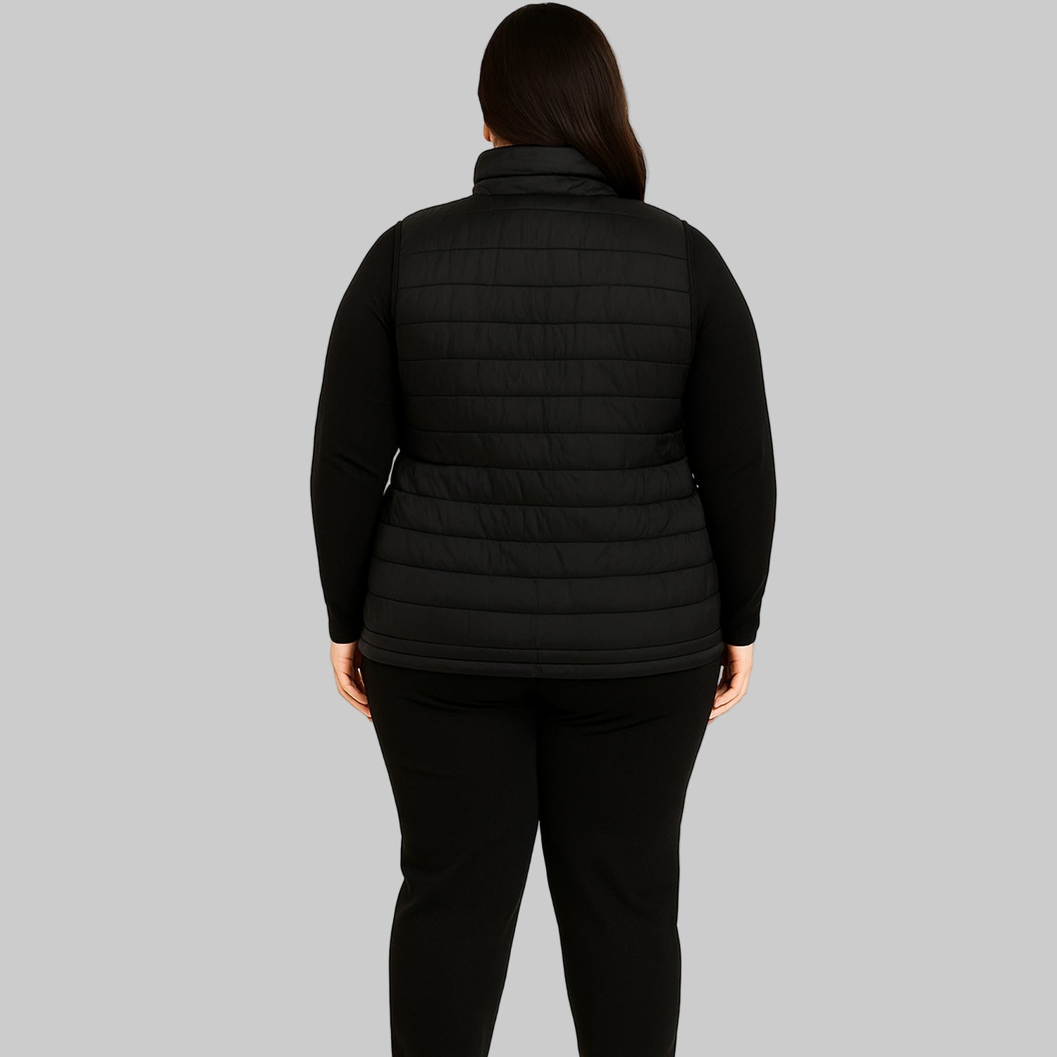Plus-size female model wearing a black short sleeveless quilted puffer jacket with a zip-front closure.