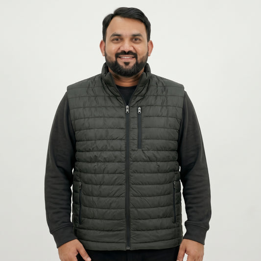 A man wearing a Black quilted zip-up vest over a black long-sleeve vest, standing against a plain grey background.