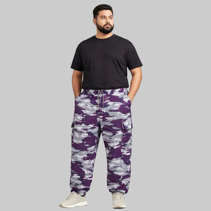 Camo Charge plus-size terry cargo pants worn by a Pakistani male model in a side pose, featuring a purple, grey, white, and black camouflage print with elastic waistband and side cargo pockets.