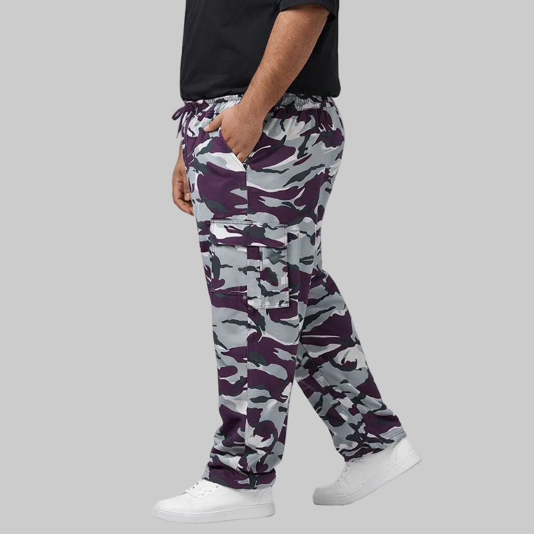 Camo Charge plus-size terry cargo pants worn by a Pakistani male model in a side pose, featuring a purple, grey, white, and black camouflage print with elastic waistband and side cargo pockets.