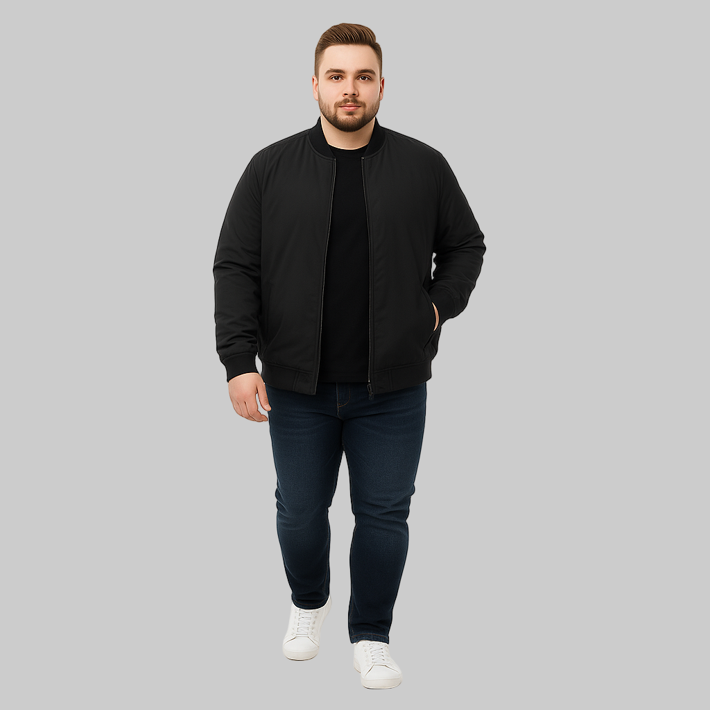Plus-size male model wearing a black bomber jacket with ribbed cuffs, hem, and welt pockets, styled with jeans and sneakers on a white studio background