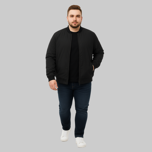 Plus-size male model wearing a black bomber jacket with ribbed cuffs, hem, and welt pockets, styled with jeans and sneakers on a white studio background