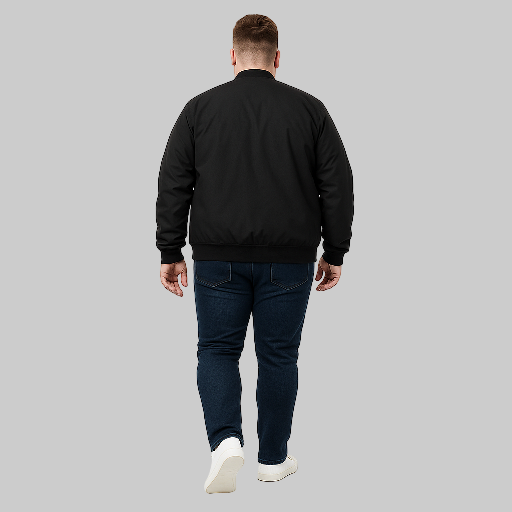 Plus-size male model wearing a black bomber jacket with ribbed cuffs, hem, and welt pockets, styled with jeans and sneakers on a white studio background