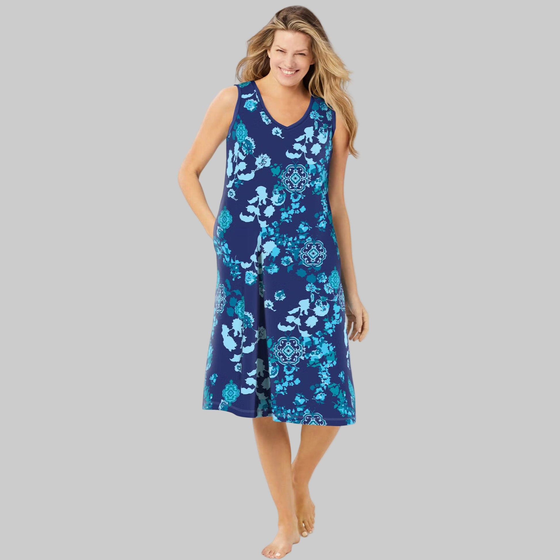 Plus-size woman wearing an evening blue sleeveless short lounger with a peony floral print, side pockets, and V-neck, on a white background.