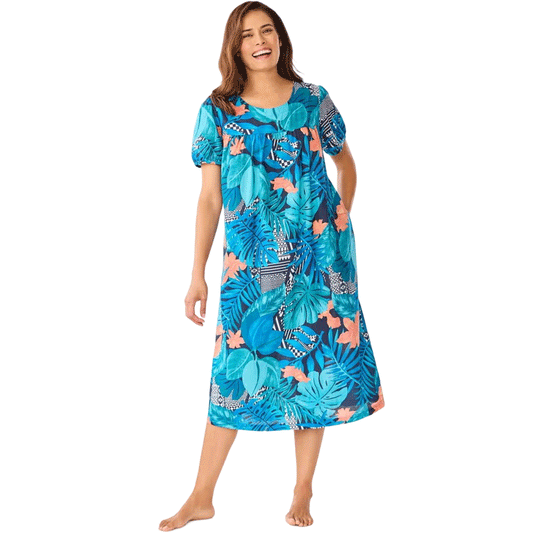 Plus-size woman wearing a short-sleeve, mid-length lounger with a paradise blue tropical geo print, featuring shirred front and back yokes and side seam pockets.