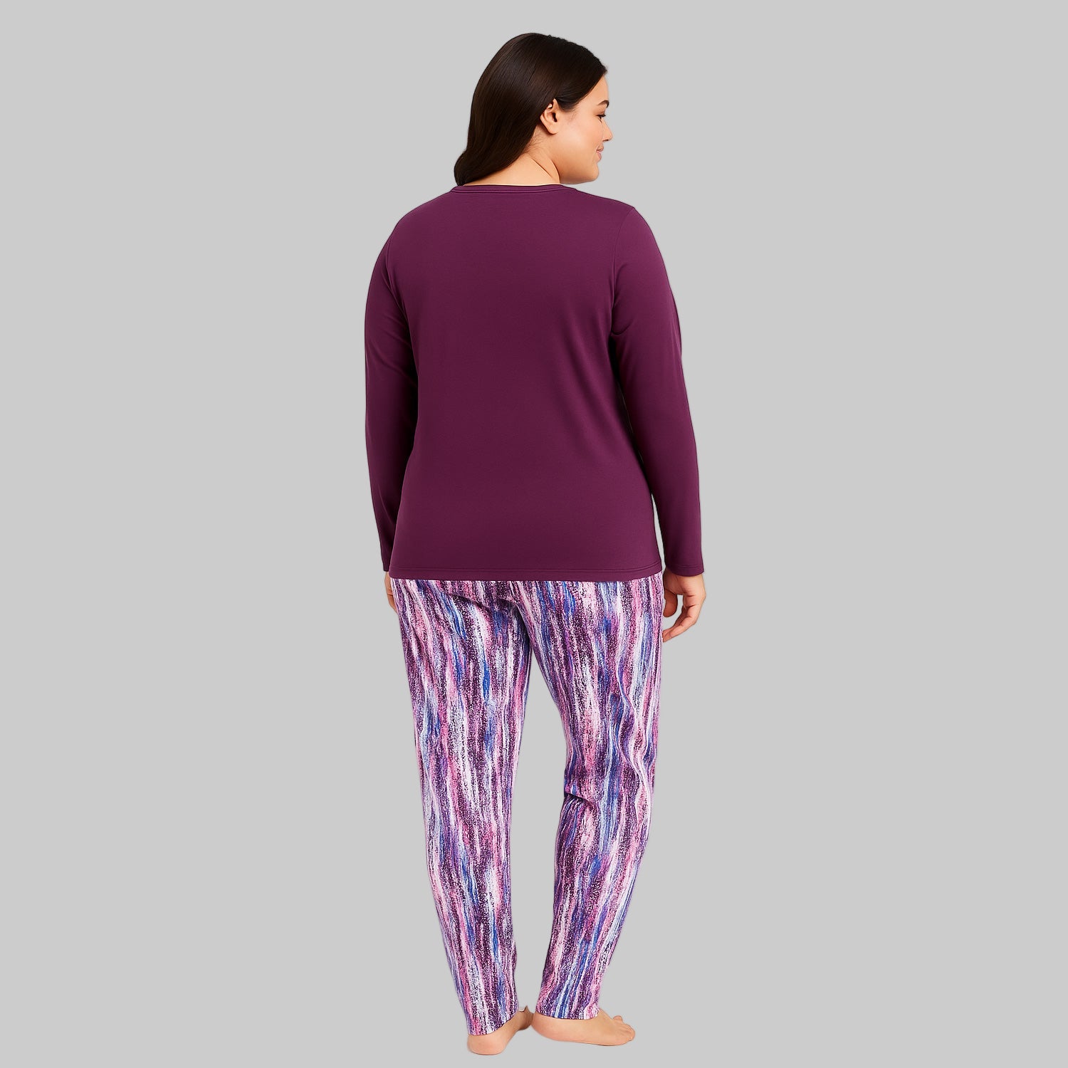 Plus-size woman wearing a plum long-sleeve pajama top with printed pocket and multicolor abstract print pajama bottoms — cozy cotton-blend sleepwear set.