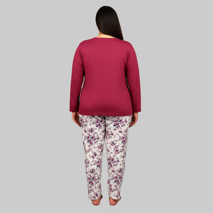 Plus-size woman wearing a plum cotton pajama set with floral white trousers and a printed pocket top on a gray studio background.