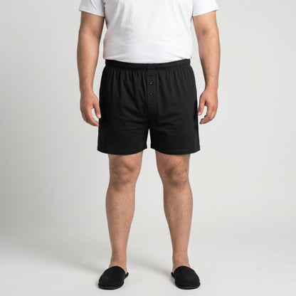 A man wearing black boxer briefs, a white t-shirt, and black slippers, standing against a light gray studio background.