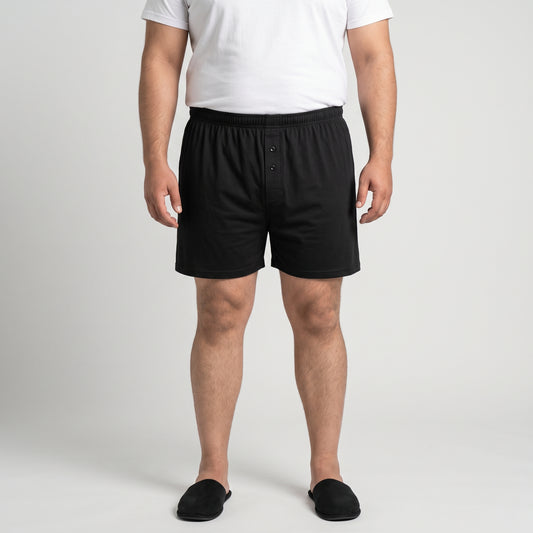 A man wearing black boxer briefs, a white t-shirt, and black slippers, standing against a light gray studio background.