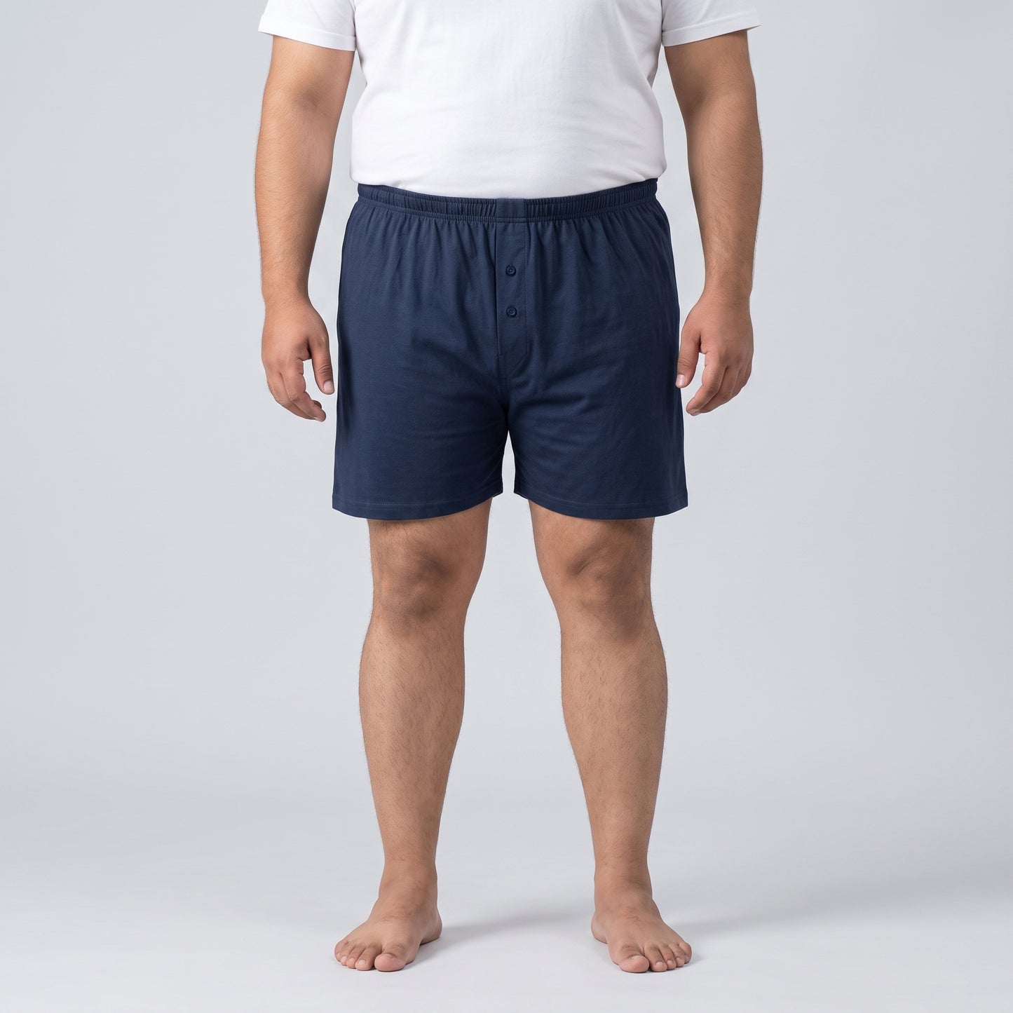 A man wearing navy blue boxer shorts and a white t-shirt, standing against a light gray studio background.