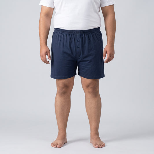 A man wearing navy blue boxer shorts and a white t-shirt, standing against a light gray studio background.