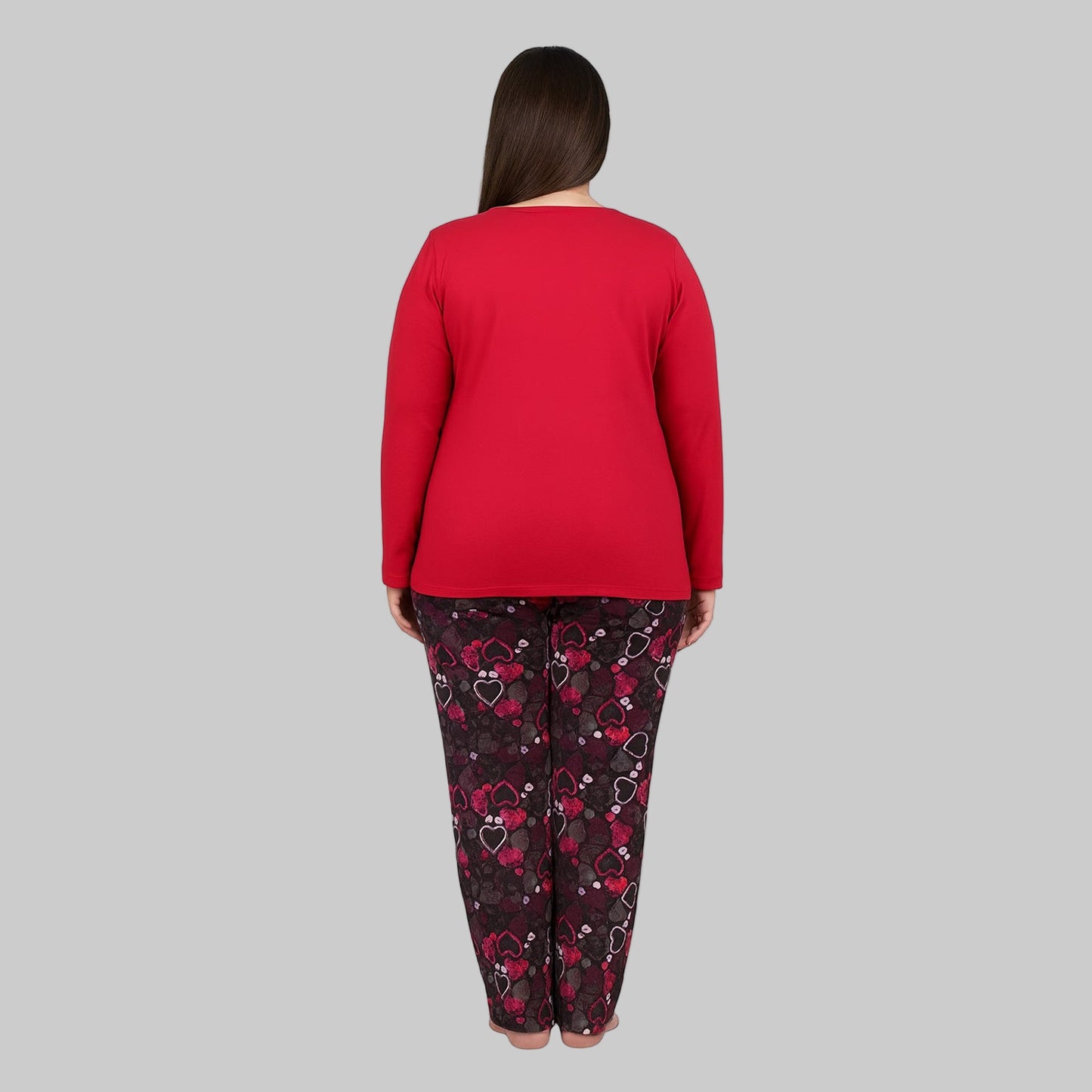Plus-size woman wearing a red long-sleeve heart print cotton pajama set with black printed trousers on a gray background.