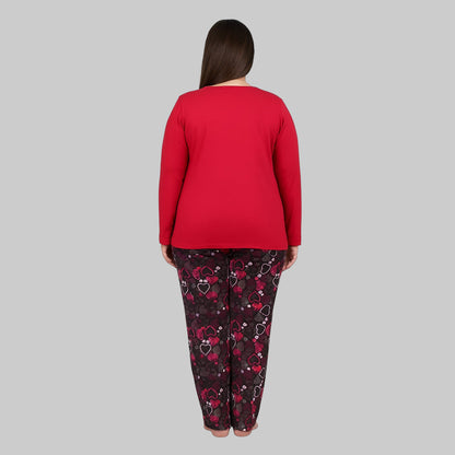 Plus-size woman wearing a red long-sleeve heart print cotton pajama set with black printed trousers on a gray background.