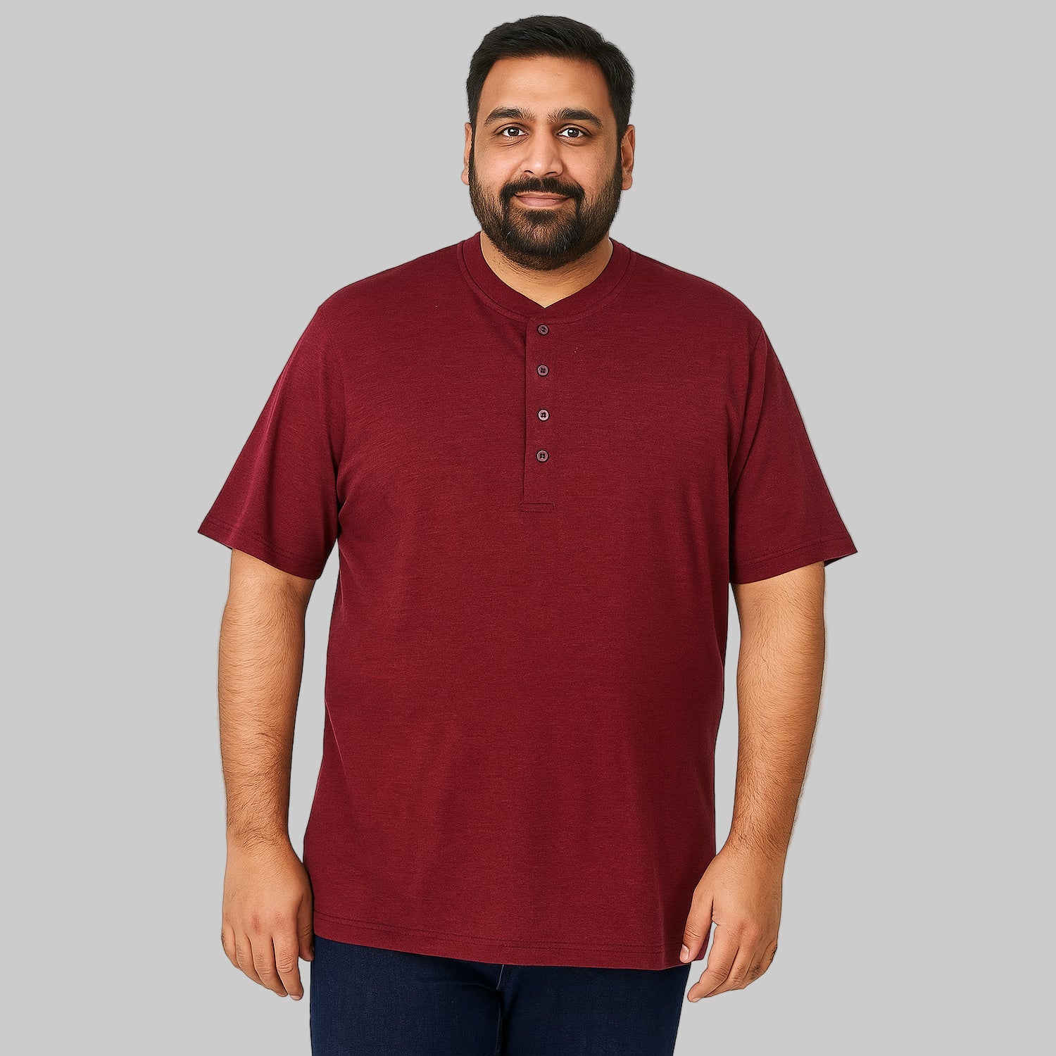 Plus-size Pakistani male model wearing rich burgundy Henley T-shirt on a light studio background, relaxed fit, 4-button placket.