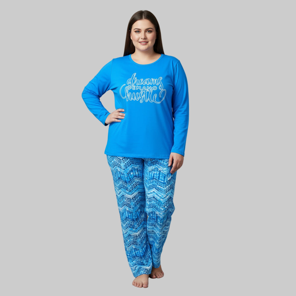 Plus-size woman wearing a sky blue “Dreams Demand Hustle” long-sleeve pajama top with blue abstract print pajama bottoms — soft cotton-blend sleepwear set.