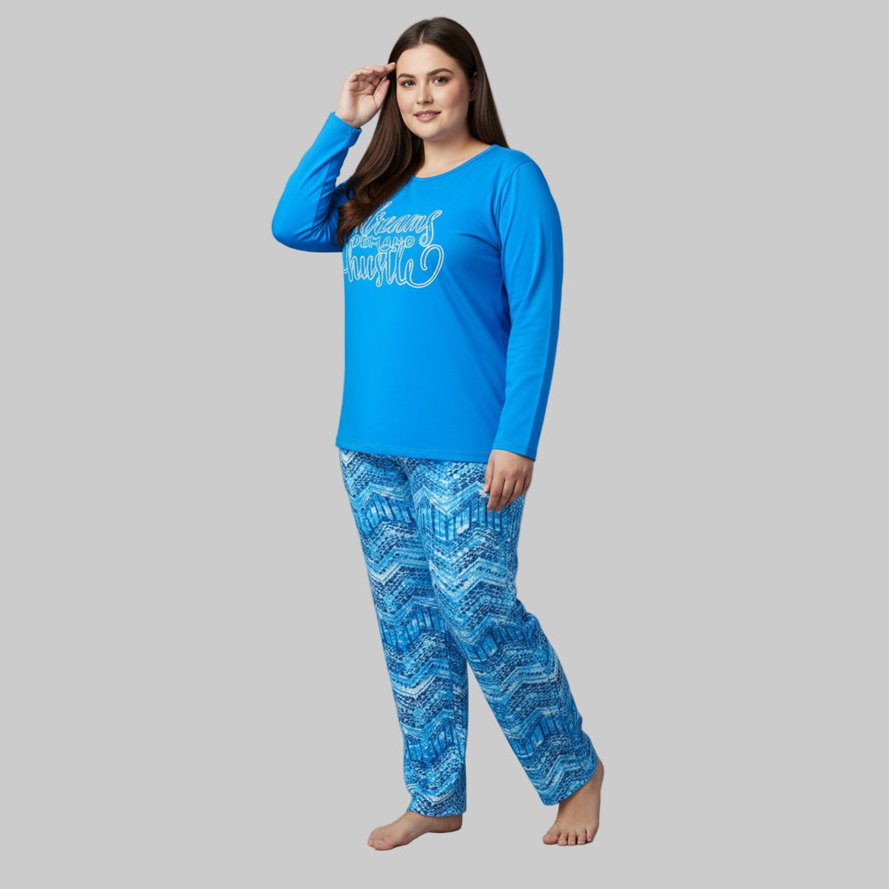 Plus-size woman wearing a sky blue “Dreams Demand Hustle” long-sleeve pajama top with blue abstract print pajama bottoms — soft cotton-blend sleepwear set.