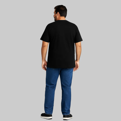 Plus-size Pakistani male model wearing black slogan graphic T-shirt on a studio background, relaxed fit, chest print visible.